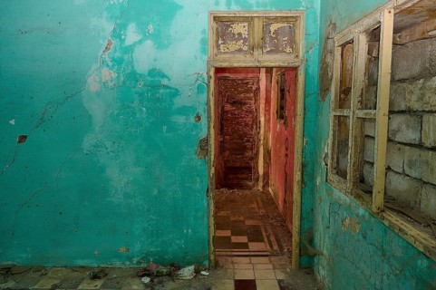 Ruined room with bright blue wall colour and destroyed door, window and a badly damaged floor,