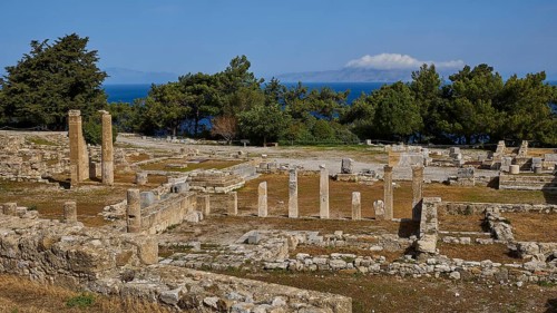 Wide angle shot of ancient ruins with stone columns and trees under blue sky, Ancient well house,