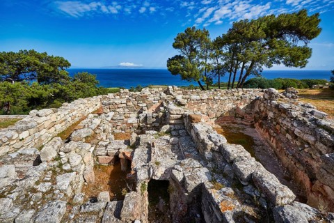 Ancient ruins with stone walls and views of the sea and trees under a blue sky, Kamiros,