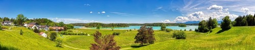 A panorama of a village on a lake with surrounding meadows and mountains, Osterseen