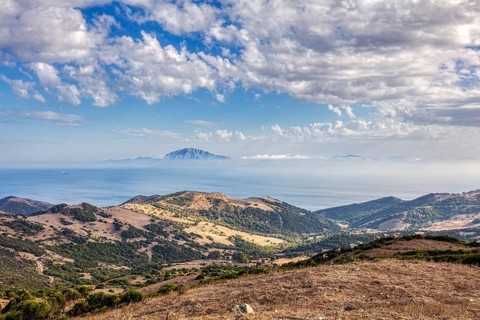 Wide landscape with mountains and sea, blue sky with clouds, near Tarifa, view to Morocco