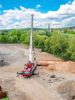 A construction site with a crane and pile of gravel, surrounded by vegetation, sky, clouds and