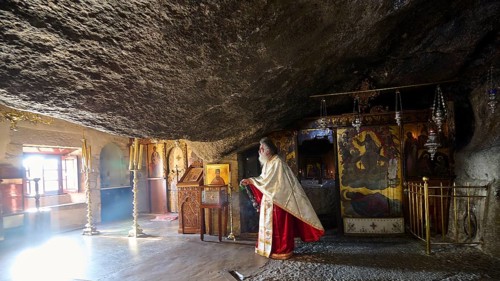 Priest in a sacred space carved into the rock in front of a decorated altar, rock grotto, Monastery
