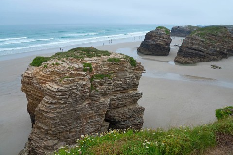 Huge rocks on the beach overlooking the sea. People walking along the shore under a cloudy sky,