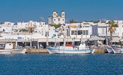 White Greek coastal town with church in the background, fishing boats in the foreground on calm sea