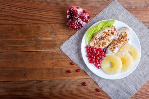 Fried chicken fillets with lettuce, pineapple and pomegranate seeds on brown wooden background,