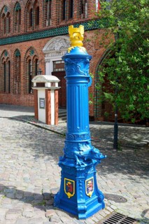 A traditional, blue-painted hydrant on a cobblestone path next to a brick building, water point,