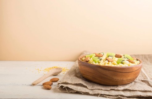 Millet porridge with kiwi and almonds in wooden bowl on a white and orange background and linen