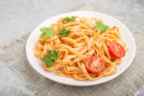 Semolina pasta with tomato pesto sauce, orange and herbs on a white ceramic plate on a gray
