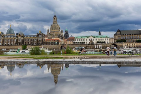 The Dresden silhouette with dark clouds behind the Church of Our Lady is reflected in a puddle on