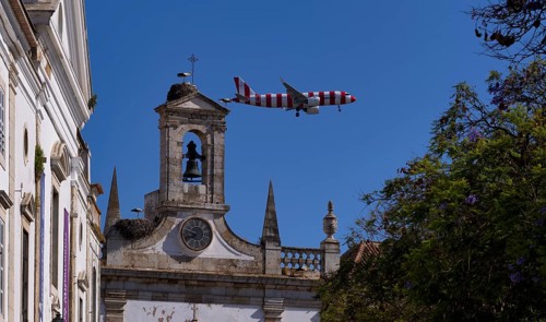 Condor holiday plane, aeroplane, flies low over city archway, stork nests, nest, storks nesting on