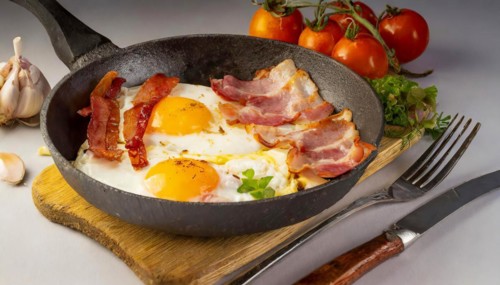 A plate of bacon, eggs, and tomatoes is on a wooden table, AI generated