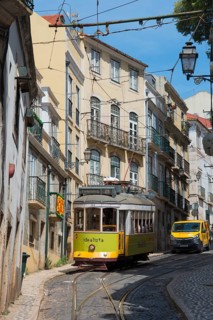 A yellow-green tram winds its way along a narrow, steep alley surrounded by old buildings, Tram,