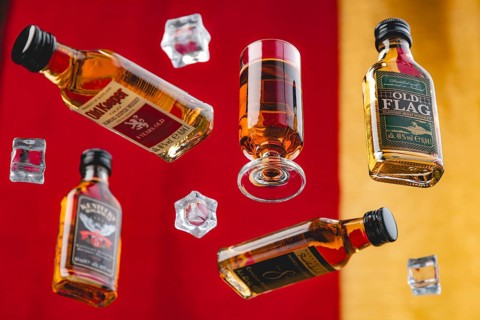 Four whisky bottles and a glass of whisky between floating ice cube cubes against a yellow and red