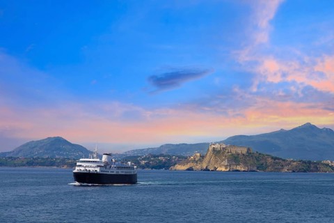 Italy, scenic sunset over Procida Island near Naples with boat approaching it from afar, Europe