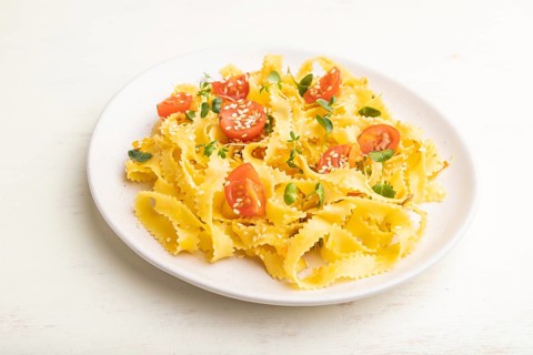 Reginelle semolina pasta with tomato, eggs, sesame and microgreen sprouts on a white wooden