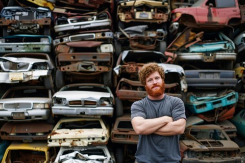 A red-haired man with a full beard, scrap dealer, in work clothes in a car junkyard, scrap yard, AI