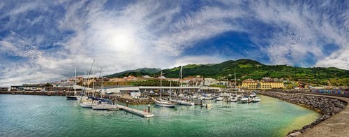 A picturesque harbour with yachts and boats, surrounded by buildings, mountains and a cloudy sky