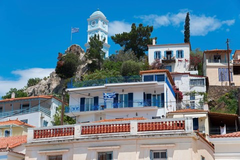 Picturesque Greek houses on a hill with a church and a Greek flag in front of it, blue and white