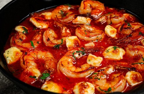 Greek saganaki, in an iron pan, saganaki with shrimp, shrimp in tomato sauce, with pepper and feta