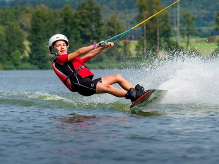 Boy or girl, happy summer holiday with wakeboard, water splashes, red life jacket, water skiing and