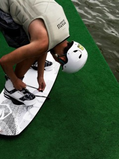 Young man with helmet and wakeboard, tying shoes in front of jump start, water sports