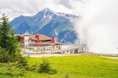 A building on a hill in front of a mountain backdrop with clouds and a green meadow, quiet and