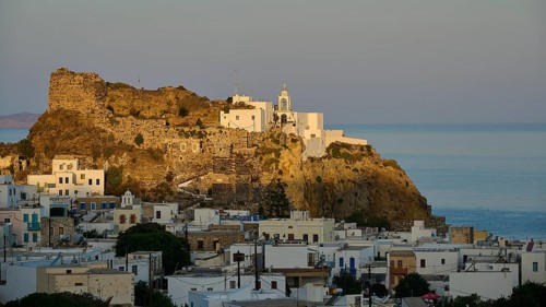 Whitewashed houses and an old castle on a hill at twilight overlooking the calm sea, morning light,