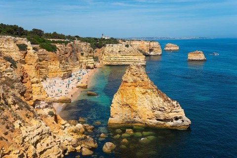 A beautiful beach on a rocky coast with clear blue water and sunny skies, Praia da Marinha, Lagoa,