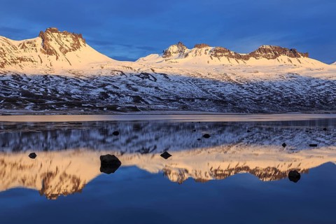 Snow-covered mountains reflected in a fjord in the evening light, Berufjördur, East Fjords,