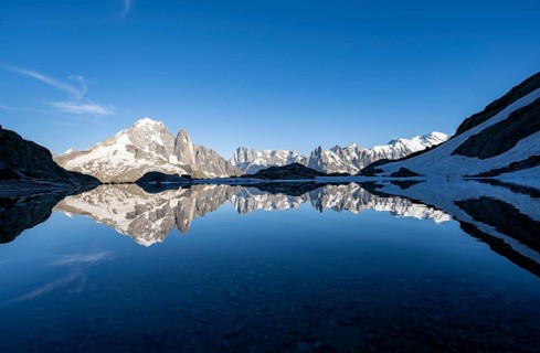 Mountaineer, silhouette in front of mountain landscape in the evening light, water reflection in