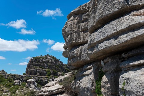 Close-up of large rocks with blue sky and clouds in the background and green vegetation, karst