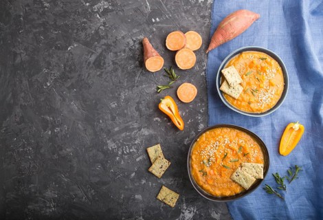 Sweet potato or batata cream soup with sesame seeds and snacks in blue ceramic bowls on a black