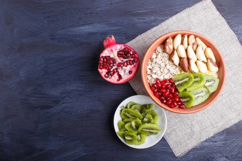 A plate with muesli, kiwi, pomegranate, Brazil nuts on a black wooden background. top view. copy