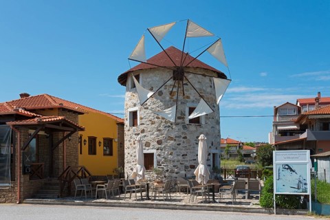 A converted windmill into a restaurant with outdoor seating under a clear blue sky, Ierissos,