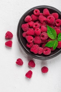 Fresh raspberries, on a black plate, with leaves, top view, on a white table