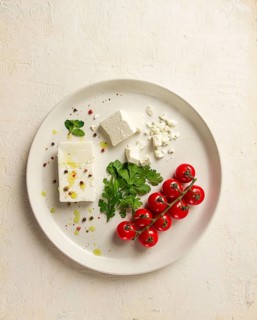 Feta cheese, for salads, with cherry, green butter, greens, on a white plate, appetizer, top view,