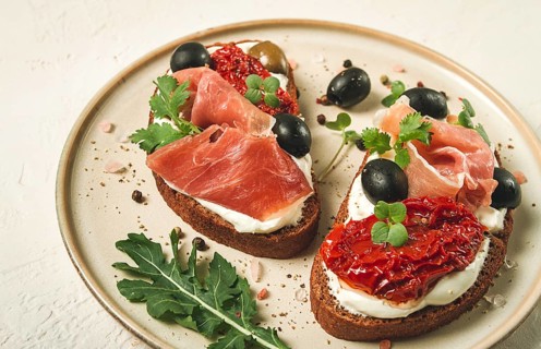 Sandwiches with cheese and prosciutto, dried tomatoes and olives, breakfast on a plate