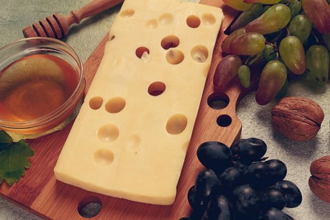 Cheese with big holes, emmental, maasdam, brie cheese, on a cutting board, with grapes and honey,