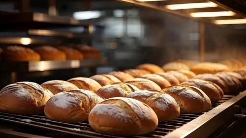 Fresh loaves of bread dominate the foreground of an industrial bakery, AI generated