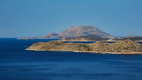 Close to a larger island in the blue sea, surrounded by blue sky and natural landscape, Makri