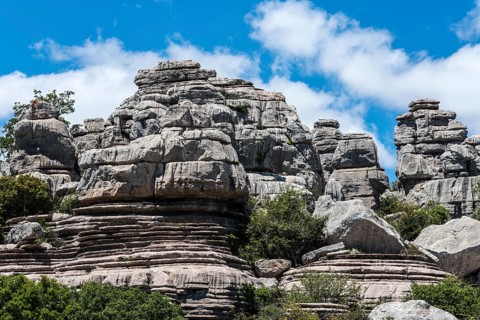 Massive rock formations under a blue sky with white clouds and green vegetation, karst mountains,