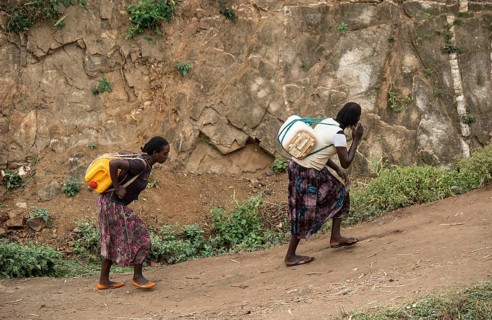 Two woman carry heavy water canisters on their backs from the water point to the village, near the