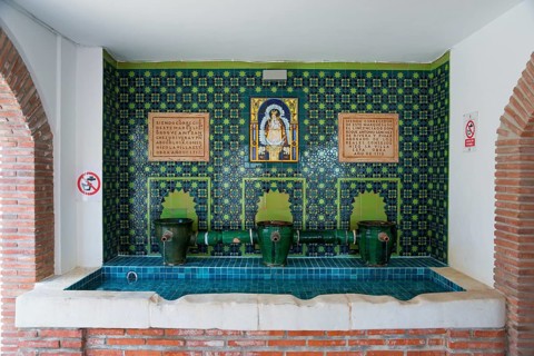 A decorated interior with blue mosaic and several taps, adorned with religious symbols and Spanish