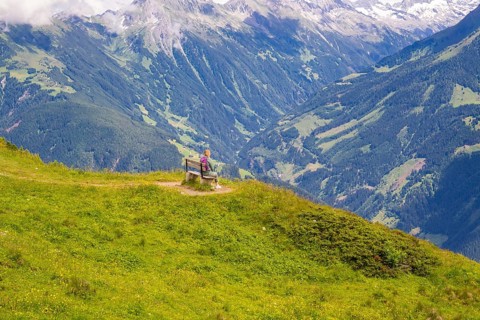 A woman sits on a bench and looks at the vast valleys and mountains, Penken, Zillertal, Austria,