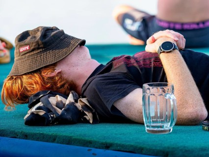Young man exhausted sleeps off, empty glass, hat over his head