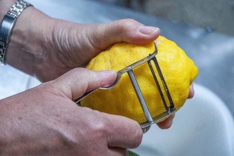 Close-up of two hands peeling a lemon during the making of limoncello, an Italian liqueur in