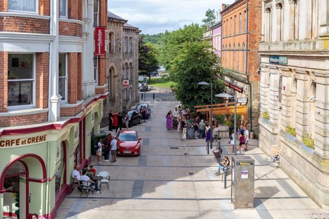 Lively pedestrianised area with cafés and shops, lined with red brick buildings and trees,