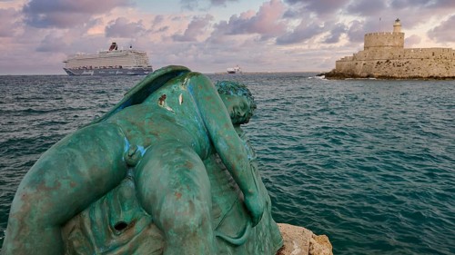A damaged sculpture looks out over the sea and a fortress during a dramatic sunset, sky exchanged,
