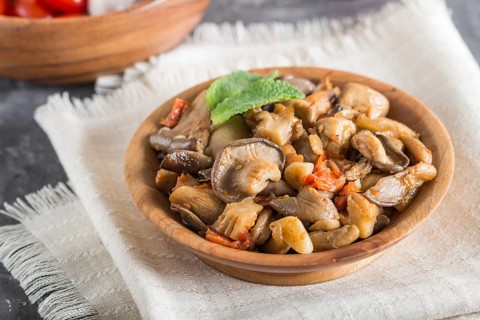 Fried oyster mushrooms with tomatoes in wooden plate on black concrete background. side view, close